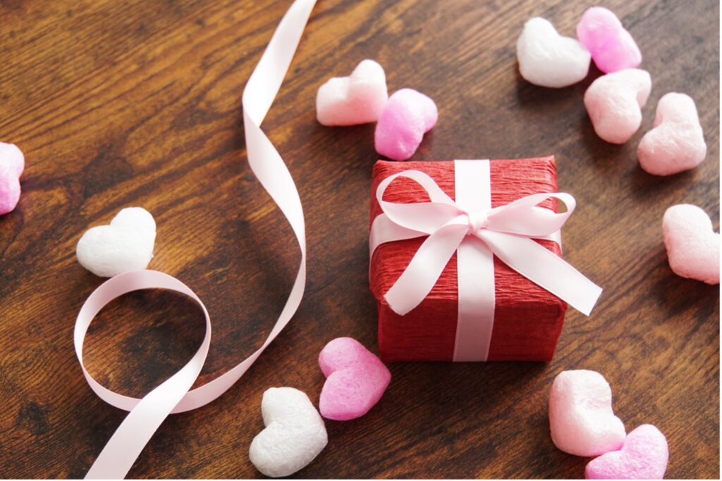 A red gift box with a pink ribbon next to hearts