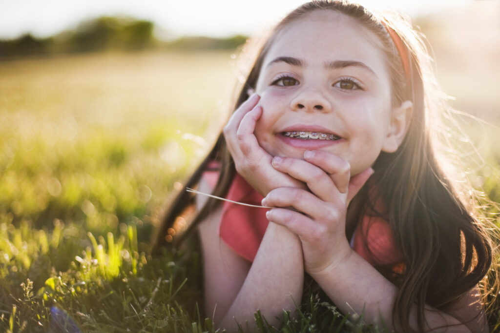 young girl lying in the grass smiling, Summer Fun with Braces