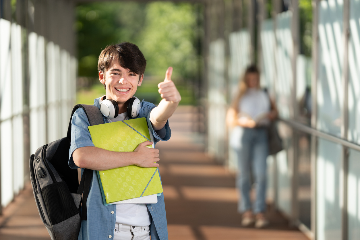 A child holding a folder and a book smiling with a thumbs up. Ace the School Year with a Smile: How Clear Aligners Can Help