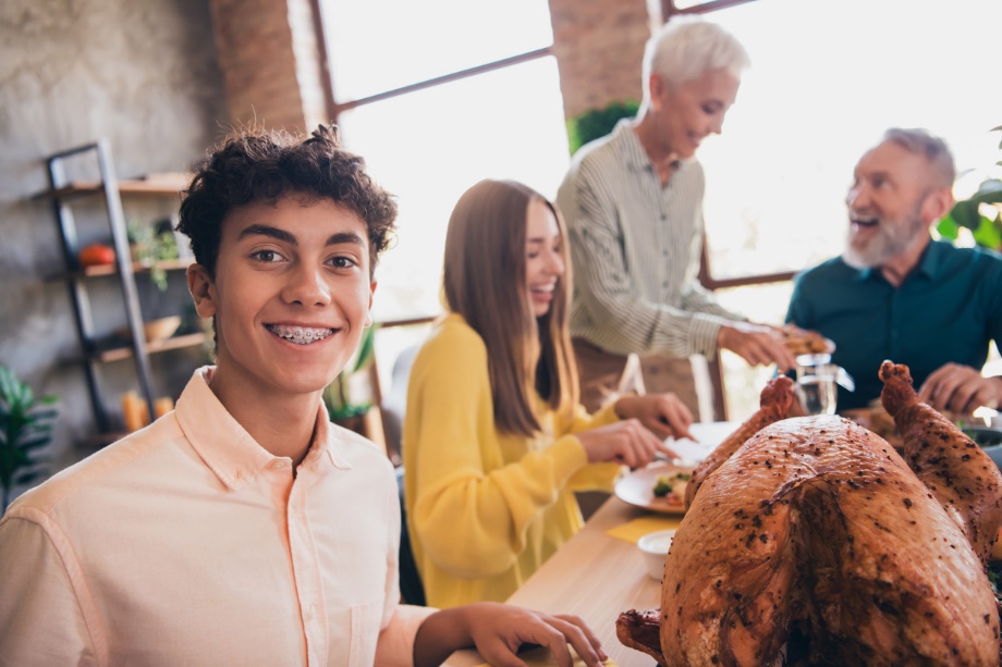 a young man smiling, A group of people eating food in the back ground, Holiday Braces & Clear Aligners Care