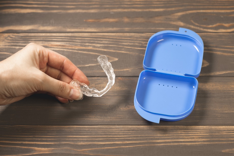 A hand holding a clear plastic retainer over a blue plastic carrying case, Holiday Braces & Clear Aligners Care