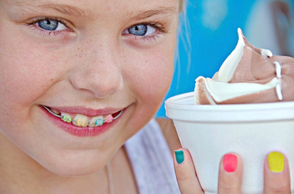 Young girl with colorful orthodontics braces and ice cream in a styrofom cup.