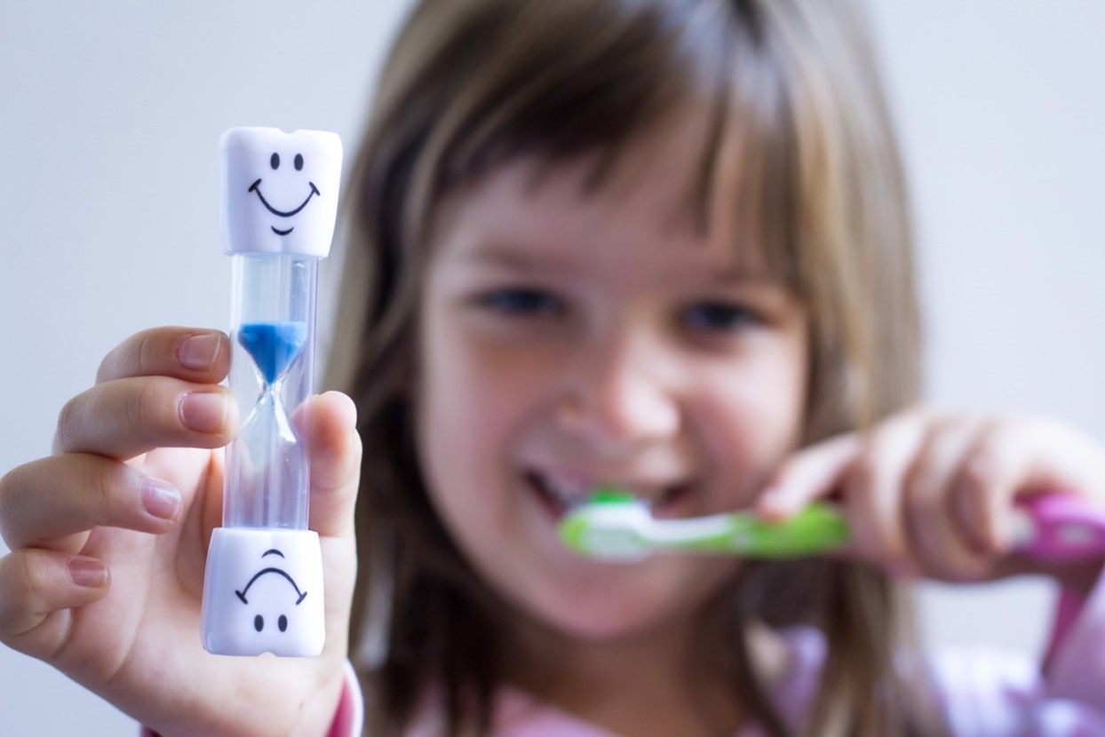 A young child holding a toothbrush and sand timer, Children's Orthodontic Care