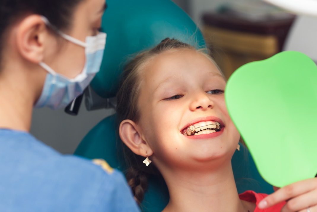 School-friendly orthodontic options, A child at the dentist looking at their braces in the mirror