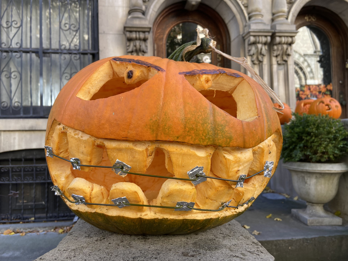 Don’t Be Spooked: Braces-Friendly Halloween Treats and Orthodontic Tips, Close-up of a smiling jack o'lantern with metal braces on the stoop of a historic townhouse in Harlem, Manhattan, New York City