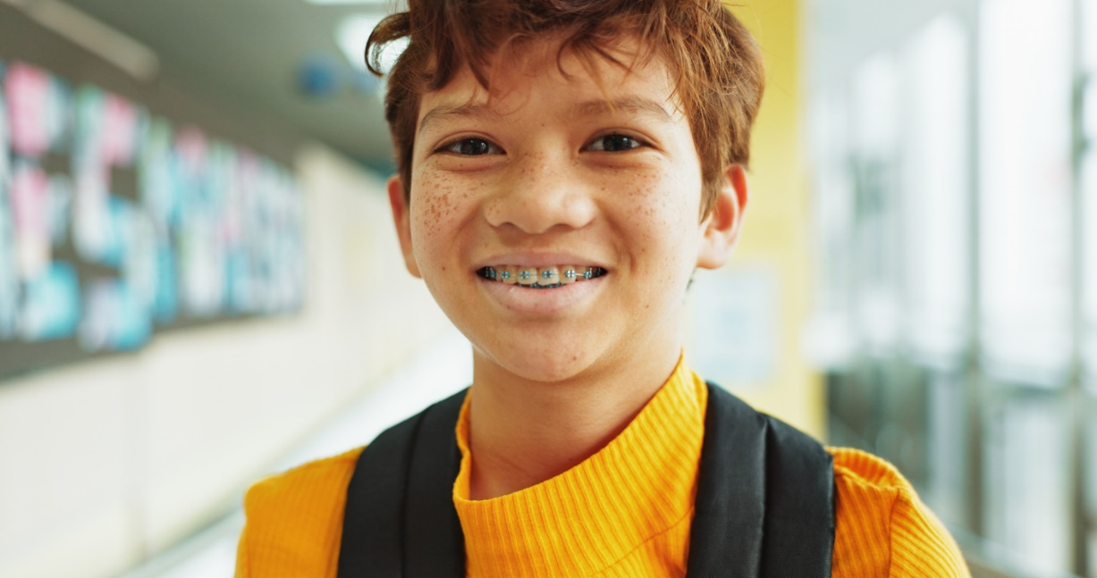 Smiling school-age boy wearing colorful braces and a backpack at school.