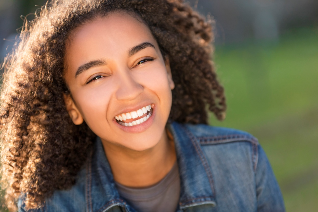 Smiling young woman showing naturally pointed upper canine teeth.